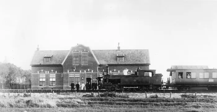 Een schitterende foto van HSM-locomotief 1059 en rijtuig 1065 aan het eindpunt Anjum. Het is duidelijk, iedereen poseert. Vermoedelijk het voltallige personeel van het station, inclusief de meid (in het witte schort). Links loeren jongens achter het hek en rechts, tussen de loc en het rijtuig, kijkt een meisje naar het voor die tijd ongetwijfeld spannende gebeuren. Fotograaf: Jacob Mosselman, Stichting Fotografie Willem Kamminga, Dokkum.