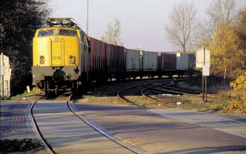 Elektrische locomotief 1216 voor een containertrein op de niet-geëlektrificeerde lijn van Leeuwarden naar Stiens op 18 november 1989. Foto: Hans Elzinga.