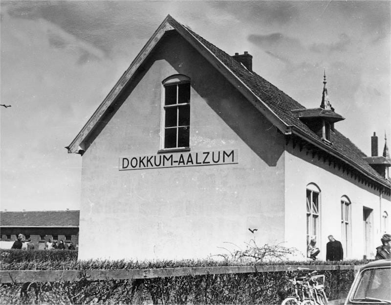 Het in 1974 afgebroken stationsgebouw van Dokkum-Aalsum kreeg tijdens de feestweek een naambord waarop de oude stationsnaam had moeten staan. De schilder maakte echter een fout in de schrijfwijze en schreef een z in plaats van een s in de benaming Dokkum-Aalsum. Hier het gebouw tijdens de NVBS-excursie op 30 april 1970 met de verkeerde naamgeving. Foto: Oege Kleijne.
