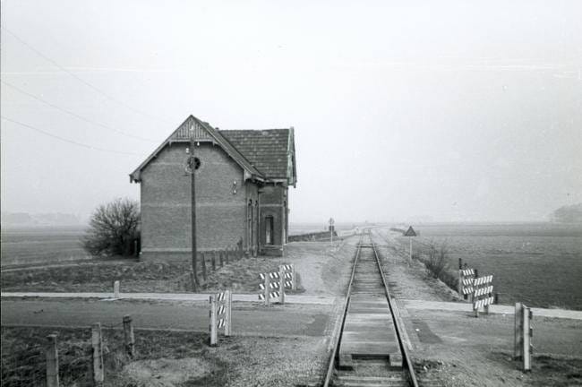 Het stationsgebouw van Hantum, gezien vanuit de richting Dokkum met overweg en bord met de maximale toegelaten baanvaksnelheid. In de jaren vijftig stonden op de meeste plaatsen nog de stationsgebouwen die tijdens de aanlegperiode, begin 1900, waren gebouwd. Tot op de dag van vandaag herinneren nog veel stationnetjes, echter zonder rails, aan de lokaalspoorperiode. Foto: Kees van de Meene, 4 april 1958.